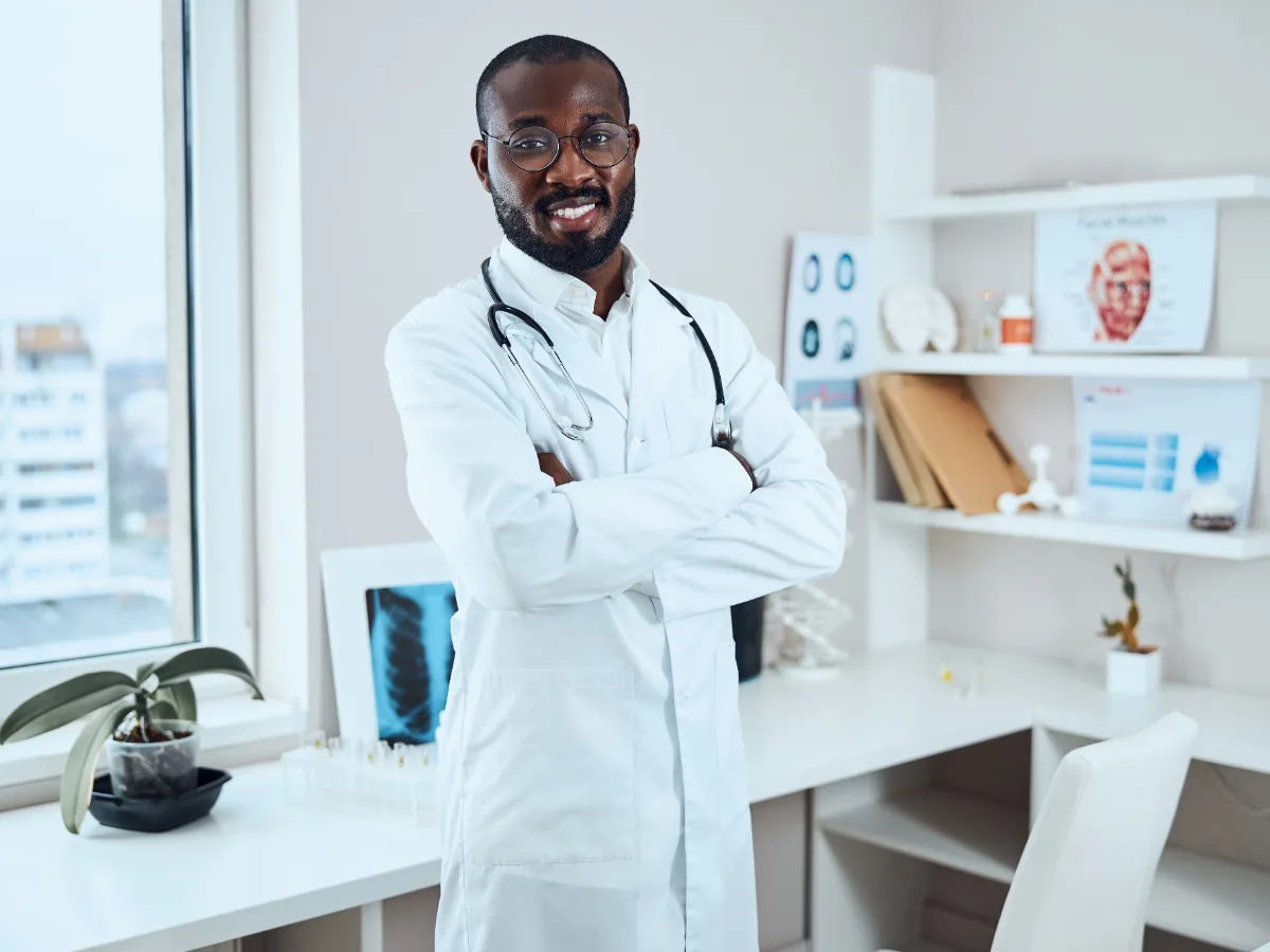 Médico jovem de braços cruzados em consultório claro e organizado — imagem ilustrativa