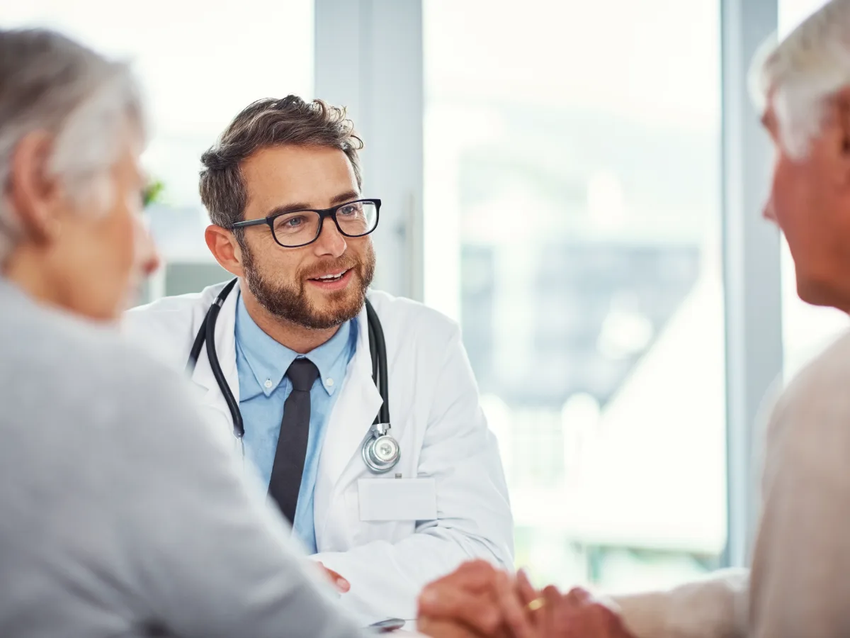 Médico conversando com casal de pacientes idosos em consultório iluminado — imagem ilustrativa
